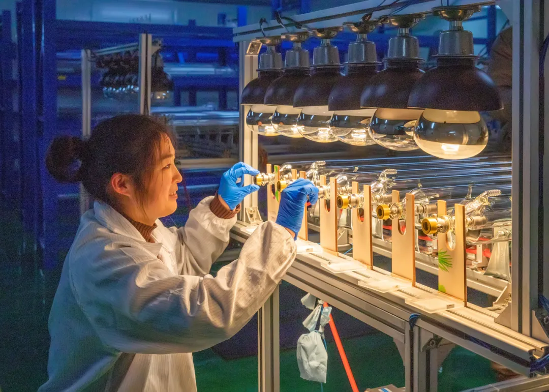 Technician fine-tuning and testing industrial CO2 laser tube optics under production heat lamps